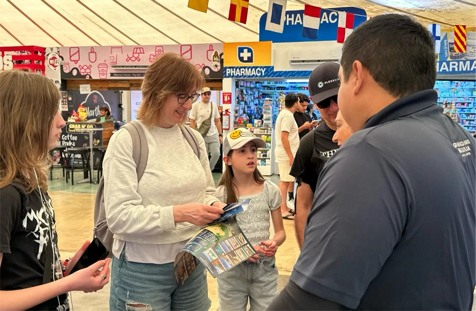 A Gran Acuario Mazatlán team member hands a brochure to a family of cruise passengers